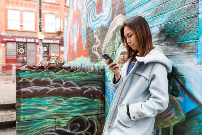 Woman leaning on wall and looking at phone